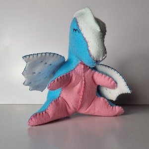 May include: A handmade plush toy dragon with blue and pink felt, white felt wings, and embroidered eyes.