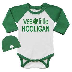 Peut inclure: Un body blanc pour bébé avec des manches et des bordures vertes, et un bonnet vert assorti. Le body porte l'inscription "wee little HOOLIGAN" en vert avec un trèfle. Une tenue festive pour la Saint-Patrick.