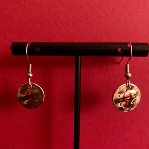 Puede incluir: Un par de pendientes de plata con un diseño de disco redondo martillado. Los discos tienen un acabado metálico rojo y dorado.
