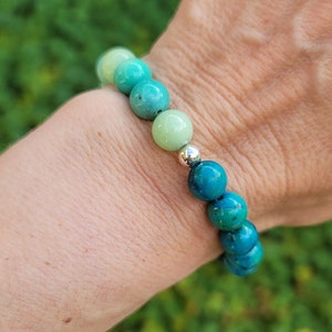 May include: A green and blue gemstone bracelet with silver beads. The bracelet is made of round beads that are graduated in size, with the largest beads at the center of the bracelet.