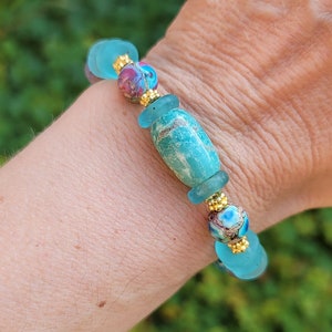 May include: A turquoise and gold beaded bracelet featuring a mix of blue and green glass beads, including a large oval-shaped turquoise bead.