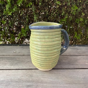 May include: A green ceramic mug with a blue rim and handle. The mug has a textured, ribbed design.