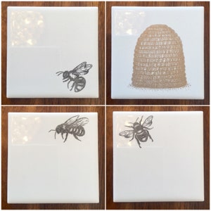 May include: Set of four white ceramic coasters with black and white illustrations of bees and a beehive. The coasters are square and have a glossy finish.