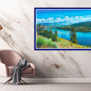 Puede incluir: Una pintura de paisaje enmarcada que representa un lago rodeado de monta&ntilde;as y &aacute;rboles. El cielo es azul con nubes blancas. El lago es de un color azul brillante.