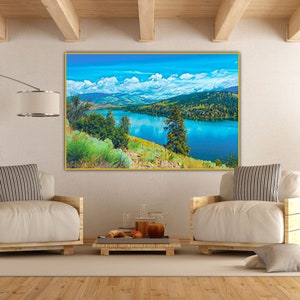 Puede incluir: Una pintura de paisaje enmarcada que representa un lago rodeado de monta&ntilde;as y &aacute;rboles. El lago es de un azul vibrante, y el cielo es de un azul brillante con nubes blancas. Las monta&ntilde;as son de un verde y marr&oacute;n suave, y los &aacute;rboles son de un verde intenso.