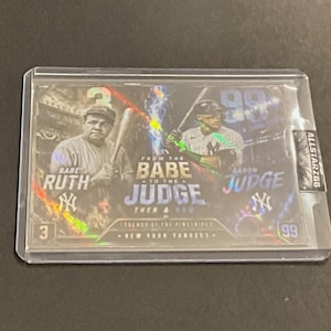 May include: A baseball trading card featuring Babe Ruth and Aaron Judge. The card has a holographic design with the text "From the Babe to the Judge" and "Legends of the Pinstripes". The card is encased in a protective sleeve.