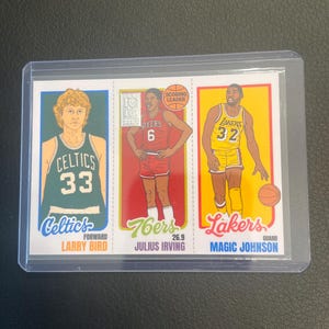 May include: A basketball trading card featuring three legendary players: Larry Bird of the Celtics, Julius Erving of the 76ers, and Magic Johnson of the Lakers. Each player is depicted in their team uniform with their name and position.