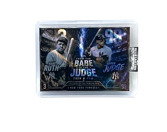 May include: A baseball trading card featuring Babe Ruth and Aaron Judge. The card has a holographic design with the text "From the Babe to the Judge" and "Legends of the Pinstripes". The card is encased in a clear protective holder.