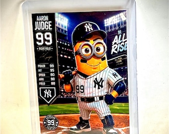 May include: A rectangular sports trading card featuring a yellow minion character dressed in a New York Yankees baseball uniform with the number 99. The card displays the text Aaron Judge, All Rise, and various player statistics on a stadium background.