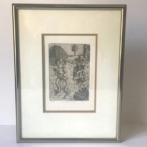 May include: Framed black and white etching depicting two figures in a rural setting. One figure plays a stringed instrument, while the other sits nearby. The artwork is set against a backdrop of a hay bale, tree, and a building, all within a silver frame.