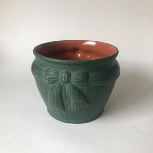 May include: A green ceramic planter with a brown rim and a raised embossed bow design.