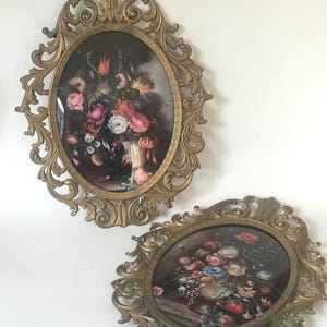 May include: Two oval-shaped framed floral prints with ornate gold frames. The prints feature bouquets of flowers in vases.