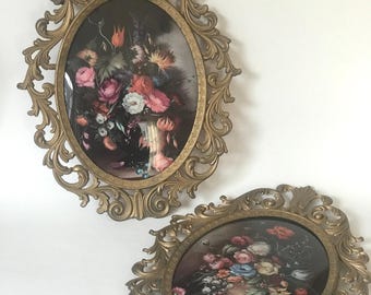 May include: Two oval-shaped framed floral prints with ornate gold frames. The prints feature bouquets of flowers in vases.