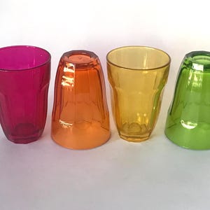 May include: Four colorful drinking glasses in shades of pink, orange, yellow, and green. Each glass has a unique shape and is made of transparent material. The glasses are arranged in a row, showcasing their vibrant colors.