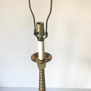 May include: A gold table lamp with a twisted base and a simple shade holder. The lamp has a white cord.