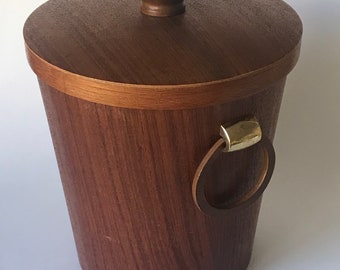 May include: A wooden ice bucket with a lid and a leather handle. The bucket is made of dark wood and has a brass ring on the handle.