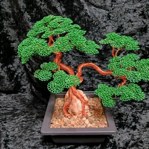 May include: A handcrafted wire bonsai tree sculpture. The tree features a copper-colored trunk and branches, with vibrant green wire leaves. It is set in a square, gray pot filled with small pebbles, creating a miniature landscape.