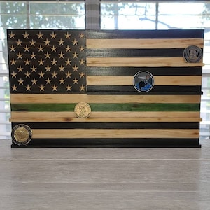May include: A wooden American flag coin display with black and green stripes. The display has five shelves for holding coins. There are three coins on the display.