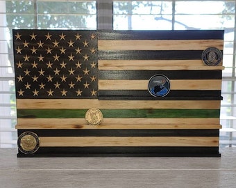 Pode incluir: Um expositor de moedas de madeira com a bandeira americana com listras pretas e verdes. O expositor tem cinco prateleiras para guardar moedas. Há três moedas no expositor.
