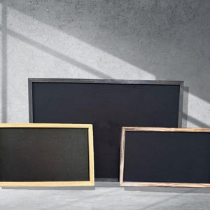 May include: Three black chalkboards with wooden frames. The largest chalkboard has a black frame, the middle chalkboard has a light wood frame, and the smallest chalkboard has a dark wood frame.