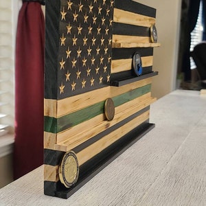 left profile of an 18x11-inch Flag. The red stripes and star field are stained black, while the white stripes have been lightly torched. The 5th strip from the bottom is stained green. There are 4 ledges to display challenge coins.