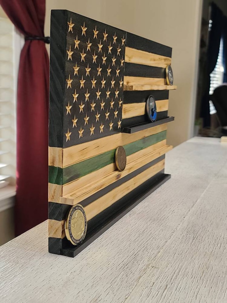 left profile of an 18x11-inch Flag. The red stripes and star field are stained black, while the white stripes have been lightly torched. The 5th strip from the bottom is stained green. There are 4 ledges to display challenge coins.