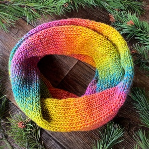 May include: A colourful knitted infinity scarf with a gradient of blue, green, yellow, orange and pink.