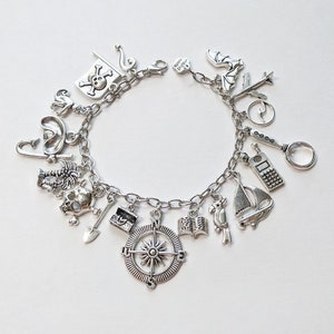 May include: Silver charm bracelet featuring various nautical and pirate-themed charms. Charms include a compass, skull and crossbones, sailboat, parrot, treasure chest, and more. The bracelet is on a white background.