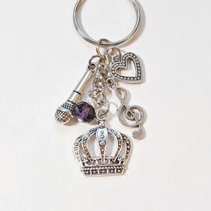 May include: Silver keychain with a crown charm, a microphone charm, a music note charm, and a heart charm. The charms are attached to a silver key ring.