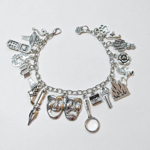 May include: A silver charm bracelet with various charms, including a quill, a magnifying glass, a boot, a key, a mask, a flame, a rose, a bird, and a phone.