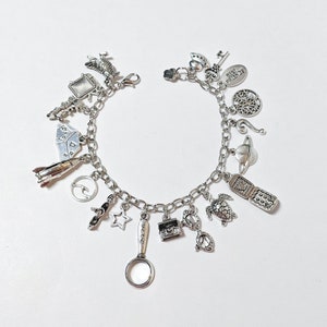 May include: Silver charm bracelet with various pendants, including a rocket, star, magnifying glass, turtle, and a flip phone. The bracelet is on a white background.
