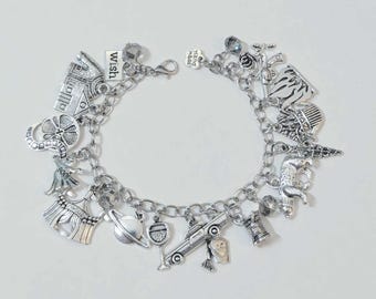 May include: Silver charm bracelet with various charms, including a house, a four-leaf clover, a planet, a wine glass, a car, and a bell. The bracelet also features charms with the words "wish" and "hand made".