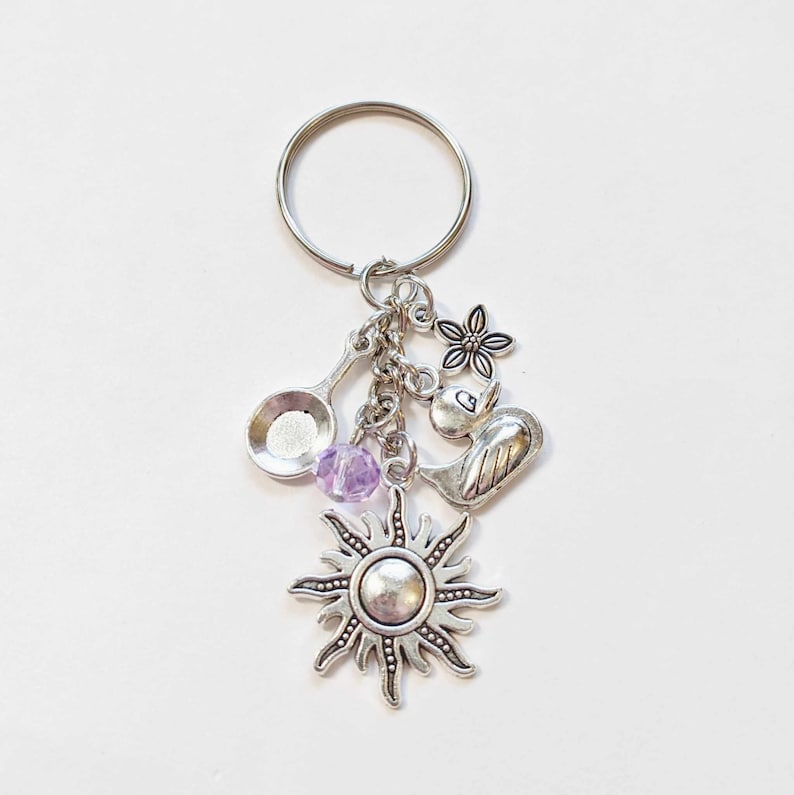 Pu&ograve; includere: Portachiavi con ciondolo in argento: un sole, un uccello, un fiore, un cucchiaio e una perla viola.