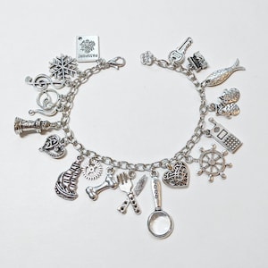May include: Silver charm bracelet featuring various charms, including a passport, snowflake, musical note, chess piece, heart, ship, gear, bone, cutlery, magnifying glass, key, fish, mittens, phone, and ship's wheel. The bracelet is on a white background.