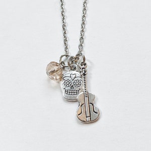 May include: A silver necklace with a sugar skull charm, a small guitar charm, and a clear crystal bead.