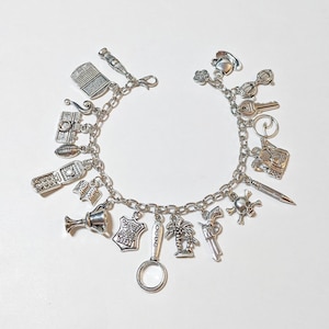 May include: Silver charm bracelet featuring various miniature charms. Charms include a laptop, camera, football, trophy, police badge, magnifying glass, palm tree, gun, skull and crossbones, and more. The bracelet is on a white background.
