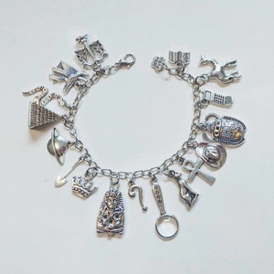 May include: Silver charm bracelet featuring various charms, including a crown, ankh, scarab beetle, pyramid, and a pharaoh. The bracelet is made of a silver chain and has a lobster clasp closure. The charms are detailed and add a unique touch to the jewelry.