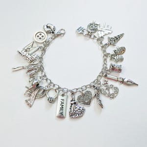 May include: Silver charm bracelet featuring various charms, including a button, a letter, a ring, a dress, and a heart. The bracelet has a chain link design and a lobster clasp closure. The word "FAMILY" is engraved on a charm.