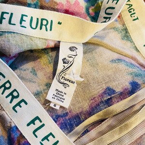 May include: A white fabric with a floral print and a green and white ribbon with the text "Terre Fleuri" on it. A white tag with the text "Floreal" and "Made in China Fabrique en Chine" is attached to the fabric.