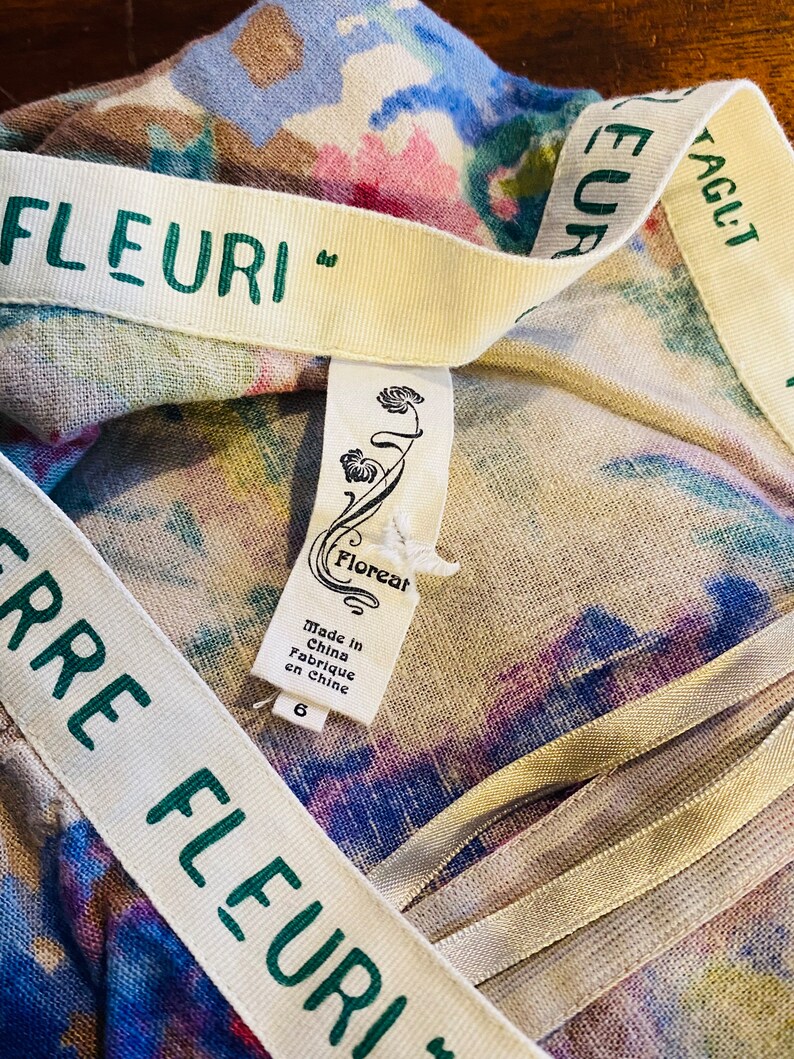 May include: A white fabric with a floral print and a green and white ribbon with the text "Terre Fleuri" on it. A white tag with the text "Floreal" and "Made in China Fabrique en Chine" is attached to the fabric.