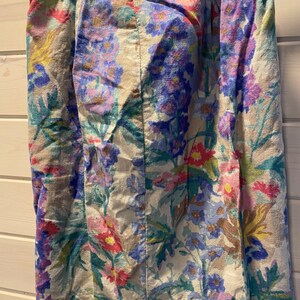 May include: A beige skirt with a floral print featuring pink, blue, and green flowers. The waistband has the text "Parterre Fleuri" in green.