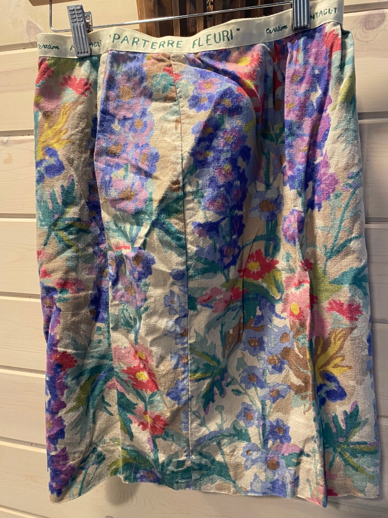 May include: A beige skirt with a floral print featuring pink, blue, and green flowers. The waistband has the text "Parterre Fleuri" in green.