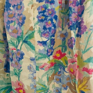 May include: A beige fabric with a floral pattern featuring blue, pink, and yellow flowers. The fabric has a subtle texture and a vintage aesthetic.
