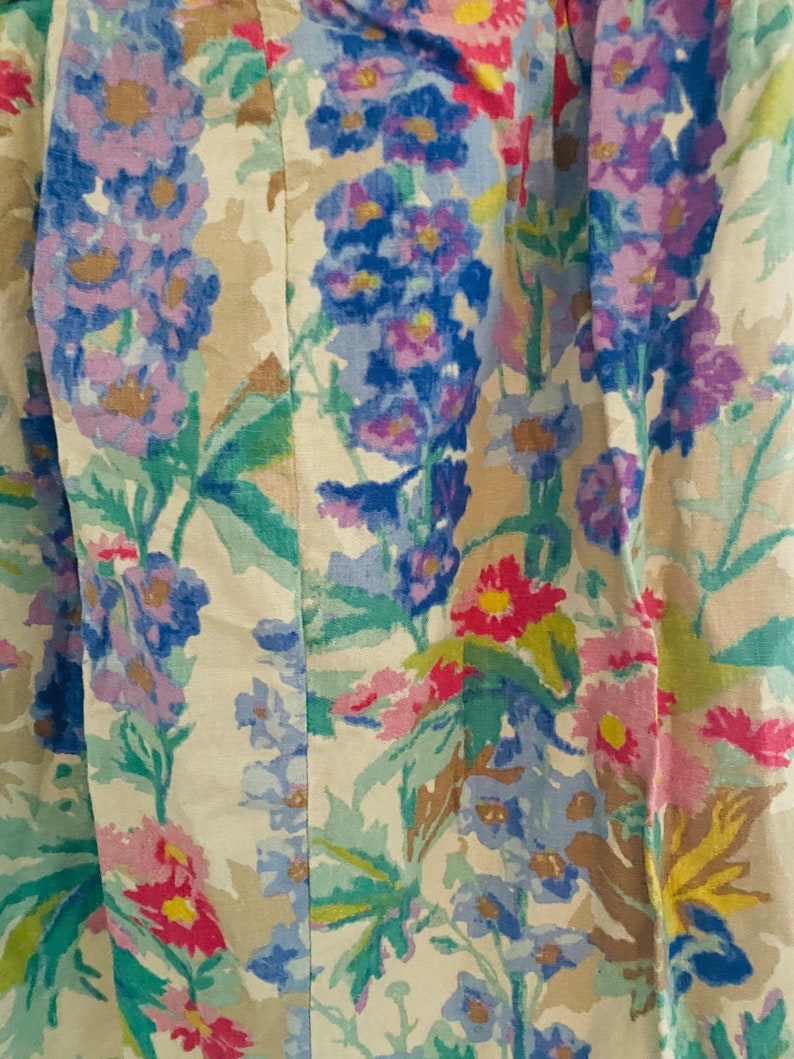 May include: A beige fabric with a floral pattern featuring blue, pink, and yellow flowers. The fabric has a subtle texture and a vintage aesthetic.