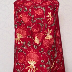 May include: A red shawl with embroidered pomegranate designs in shades of orange, yellow, and brown. The shawl has a paisley border and fringe.