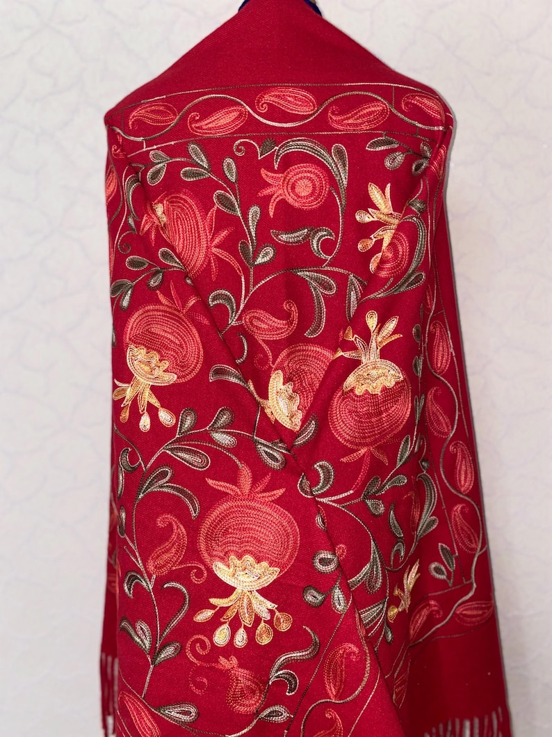 May include: A red shawl with embroidered pomegranate designs in shades of orange, yellow, and brown. The shawl has a paisley border and fringe.