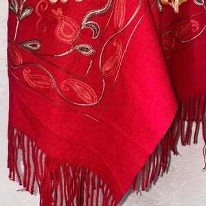 May include: Red shawl with embroidered floral and paisley designs. The shawl has a fringe border.