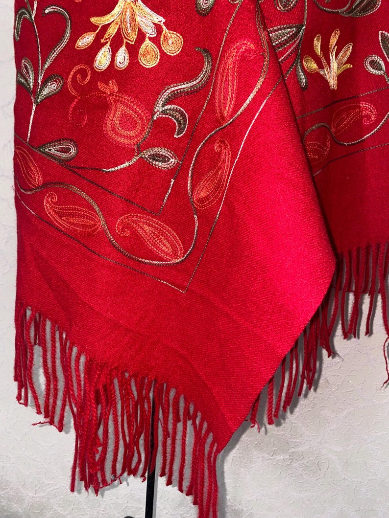 May include: Red shawl with embroidered floral and paisley designs. The shawl has a fringe border.