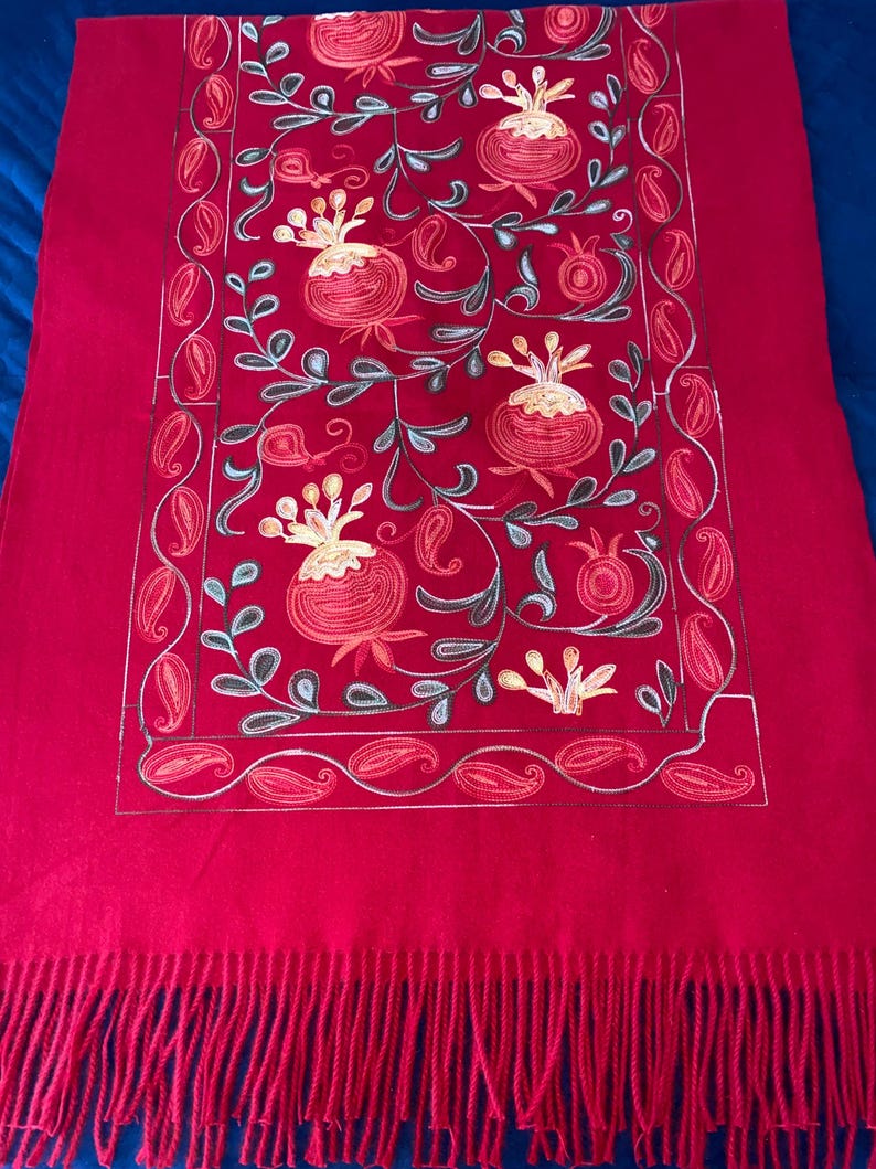 May include: A red wool shawl with embroidered pomegranate designs in shades of gold, green, and orange. The shawl has a fringe border.