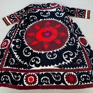 Pode incluir: Uma longa túnica preta e branca com um desenho floral vermelho e rosa. A túnica tem um motivo central redondo com um padrão repetitivo de espirais e flores.
